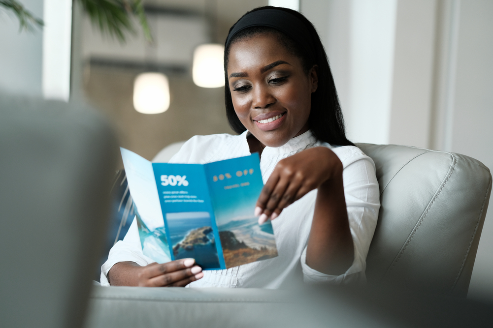 Woman smiling while reading a holiday postcard offering 50% off travel deals.